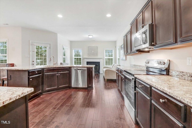 kitchen with stainless steel appliances, dark brown cabinets, a sink, and dark wood finished floors