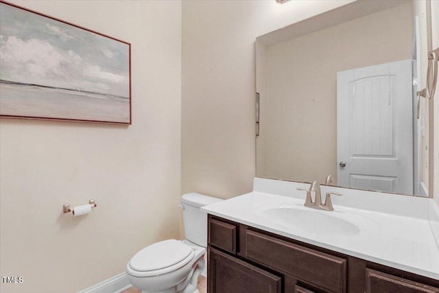 half bathroom with toilet, baseboards, and vanity