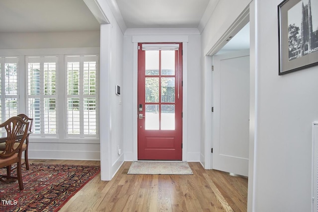 entryway with light wood finished floors, baseboards, and ornamental molding