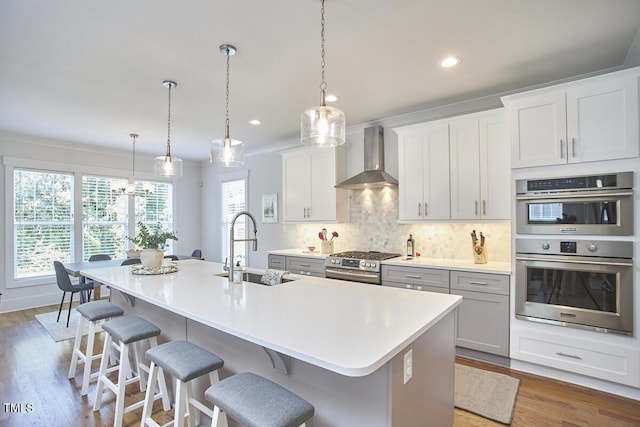 kitchen featuring tasteful backsplash, an island with sink, appliances with stainless steel finishes, wall chimney range hood, and a sink