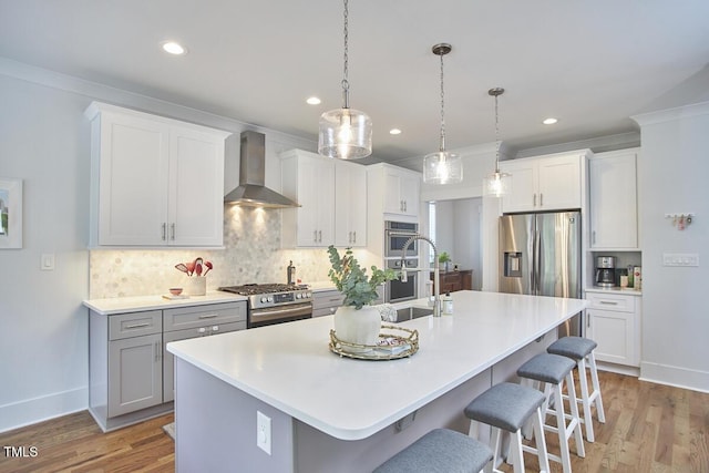 kitchen featuring an island with sink, wall chimney range hood, a breakfast bar area, and stainless steel appliances