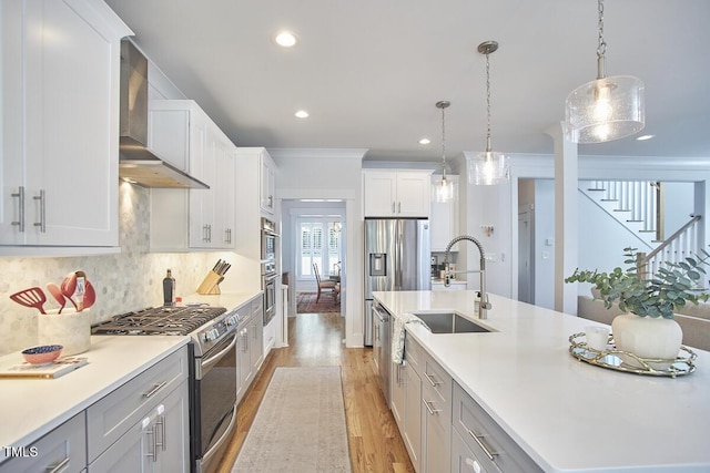 kitchen featuring stainless steel appliances, a sink, wall chimney range hood, decorative backsplash, and an island with sink