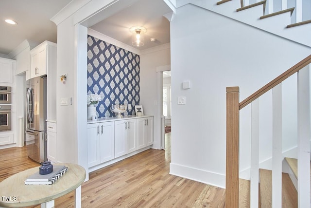 kitchen with crown molding, stainless steel appliances, light countertops, white cabinetry, and light wood-type flooring