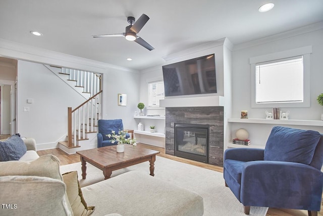 living room with stairs, a tiled fireplace, wood finished floors, and crown molding