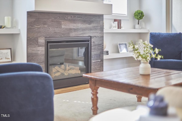 interior space with built in shelves, a glass covered fireplace, and wood finished floors