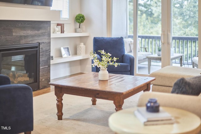 living room with built in shelves, a glass covered fireplace, and wood finished floors