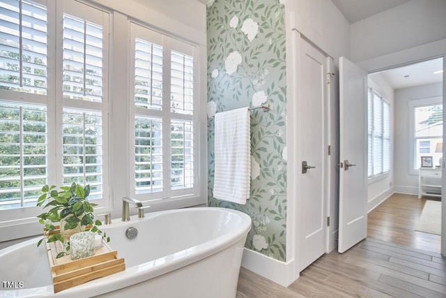 bathroom featuring baseboards, wood finished floors, a freestanding tub, and wallpapered walls