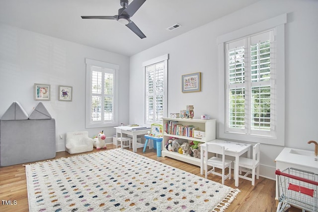 recreation room with baseboards, ceiling fan, visible vents, and wood finished floors