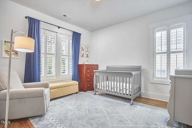 bedroom with baseboards, multiple windows, visible vents, and wood finished floors