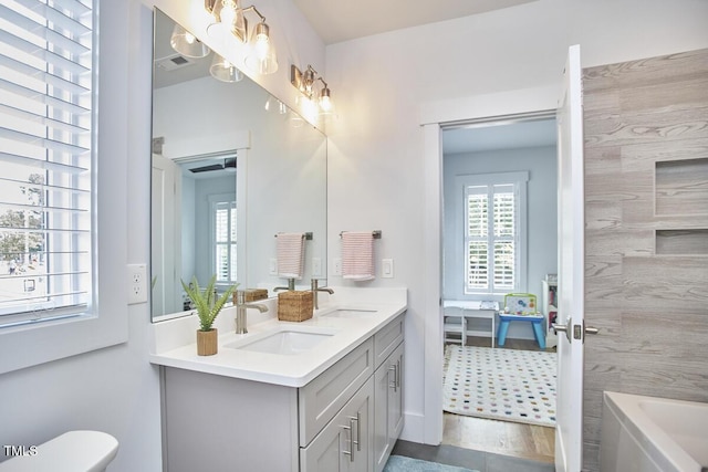 bathroom with a bath, double vanity, a sink, and toilet