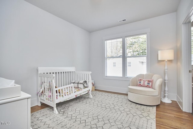 bedroom featuring a nursery area, visible vents, baseboards, and wood finished floors