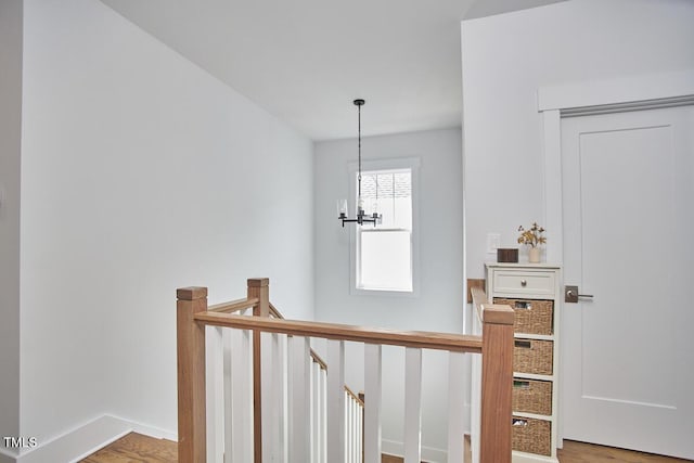 corridor featuring baseboards, wood finished floors, a notable chandelier, and an upstairs landing