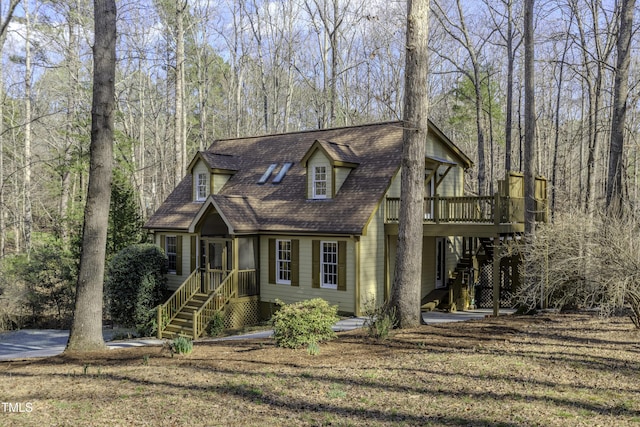 view of front of home with a deck, a wooded view, and a shingled roof