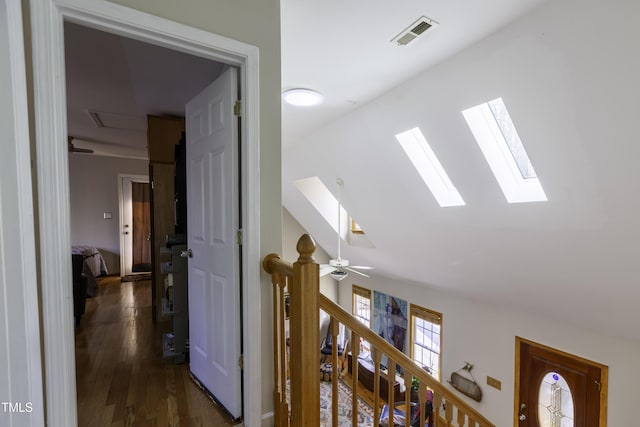 hallway featuring lofted ceiling with skylight, visible vents, an upstairs landing, and dark wood-type flooring