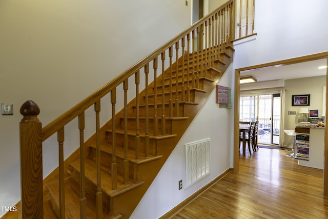 stairway featuring wood finished floors, visible vents, and a towering ceiling