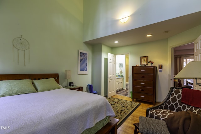 bedroom featuring baseboards, light wood-style flooring, a high ceiling, recessed lighting, and connected bathroom