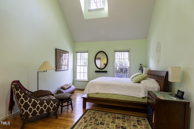 bedroom with a skylight, wood finished floors, and high vaulted ceiling