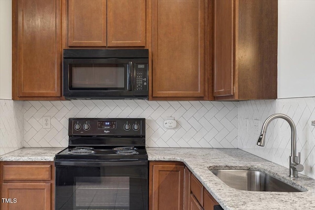 kitchen featuring light stone countertops, black appliances, backsplash, and a sink