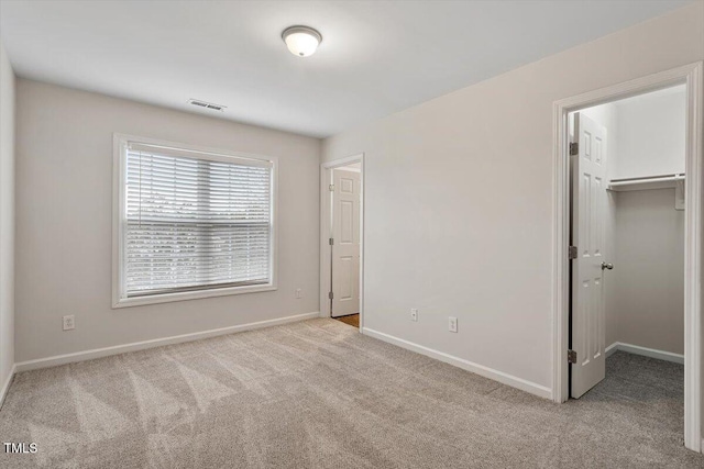 unfurnished bedroom with carpet floors, visible vents, baseboards, a closet, and a walk in closet