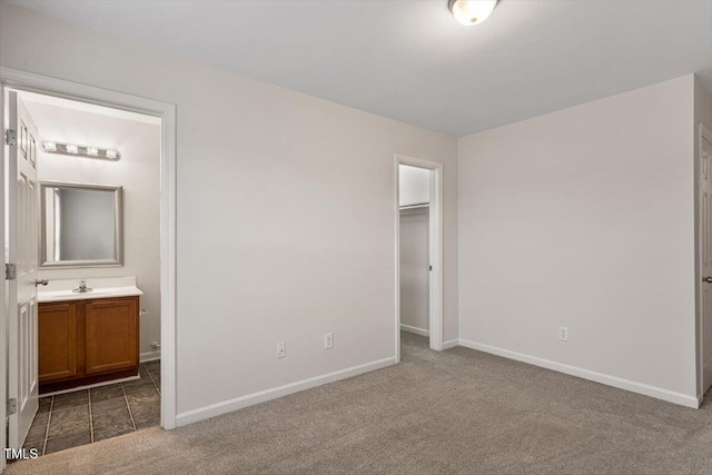 unfurnished bedroom with connected bathroom, carpet floors, baseboards, a closet, and a walk in closet