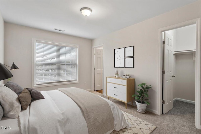 bedroom featuring light carpet, a walk in closet, visible vents, and baseboards