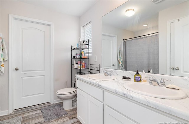 bathroom with toilet, double vanity, a sink, and wood finished floors