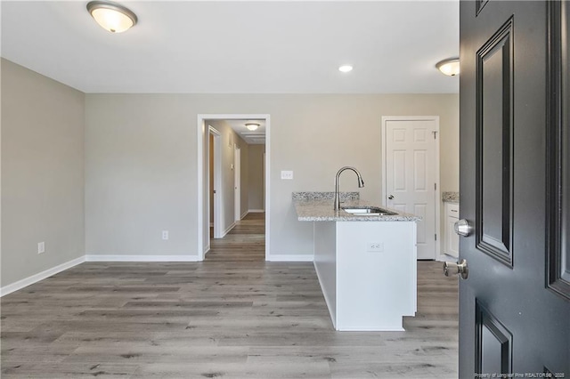 kitchen featuring light wood-type flooring, a sink, light stone counters, a peninsula, and baseboards