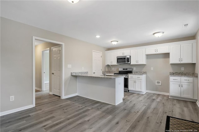 kitchen with a peninsula, white cabinets, light wood-type flooring, and stainless steel appliances