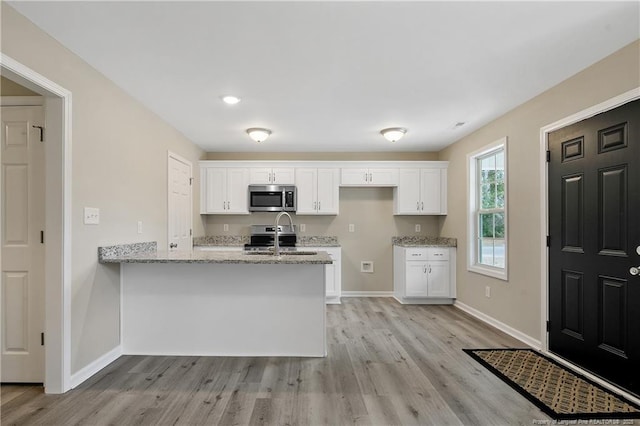 kitchen with stainless steel microwave, white cabinets, a peninsula, and a sink