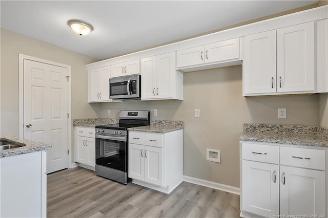 kitchen featuring light wood finished floors, appliances with stainless steel finishes, white cabinetry, and light stone counters