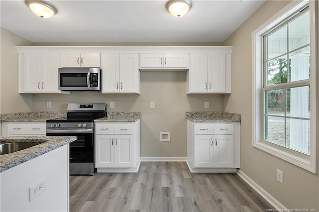 kitchen with light wood-style flooring, light stone counters, white cabinetry, appliances with stainless steel finishes, and baseboards