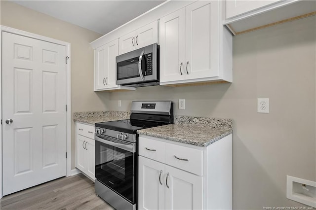 kitchen with white cabinets, appliances with stainless steel finishes, light wood-style flooring, and light stone countertops