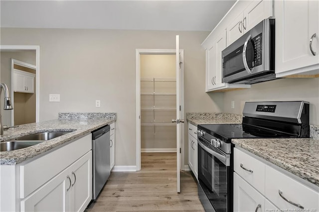 kitchen featuring light wood-type flooring, a sink, white cabinetry, appliances with stainless steel finishes, and light stone countertops