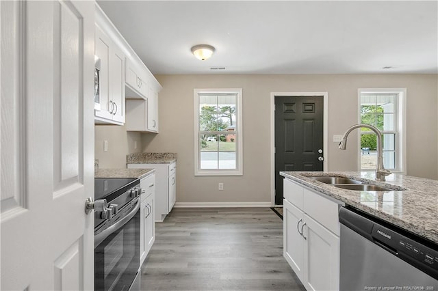 kitchen with white cabinets, light stone countertops, stainless steel appliances, and a sink