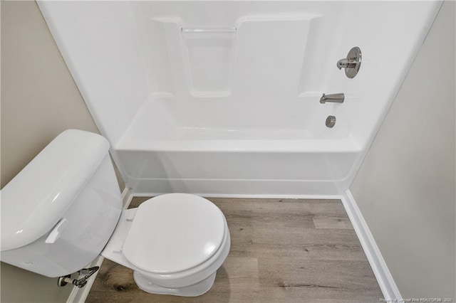 bathroom with bathing tub / shower combination, toilet, wood finished floors, and baseboards