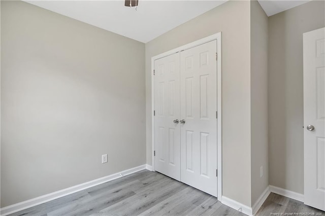 unfurnished bedroom featuring a closet, light wood-type flooring, and baseboards