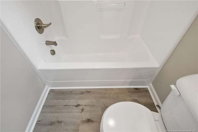 bathroom with baseboards, toilet, wood finished floors, and bathing tub / shower combination