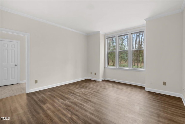 empty room with ornamental molding, wood finished floors, visible vents, and baseboards