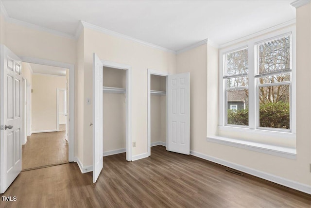 unfurnished bedroom featuring ornamental molding, wood finished floors, visible vents, and multiple closets