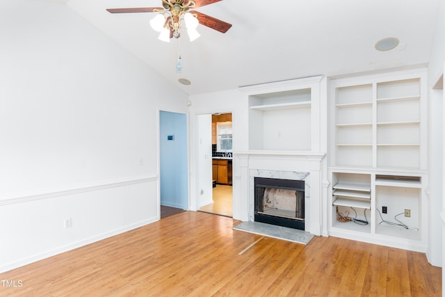 unfurnished living room with a high end fireplace, baseboards, vaulted ceiling, a ceiling fan, and light wood finished floors