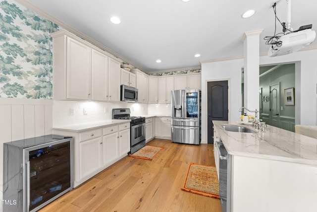 kitchen with wine cooler, a wainscoted wall, a sink, appliances with stainless steel finishes, and light wood-type flooring