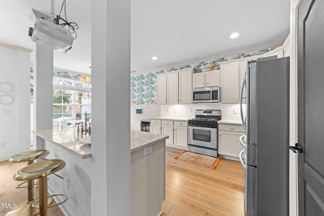 kitchen featuring white cabinets, a kitchen breakfast bar, stainless steel appliances, light wood-style floors, and backsplash