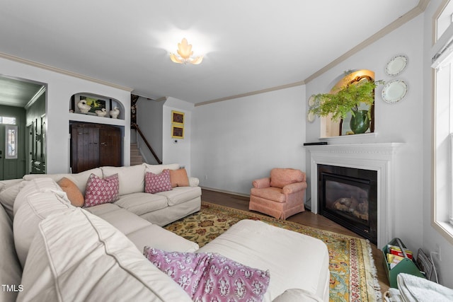 living room with stairs, ornamental molding, wood finished floors, and a glass covered fireplace