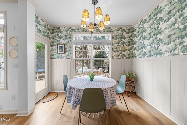 dining area featuring crown molding, light wood-style flooring, wainscoting, a chandelier, and wallpapered walls