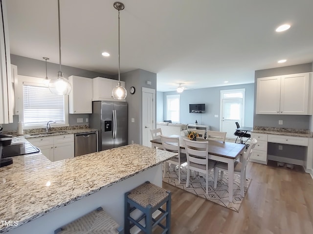 kitchen featuring stainless steel appliances, light wood-style flooring, a peninsula, and light stone countertops