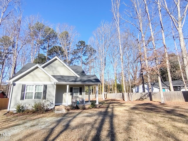 view of front facade featuring covered porch, a shingled roof, and fence