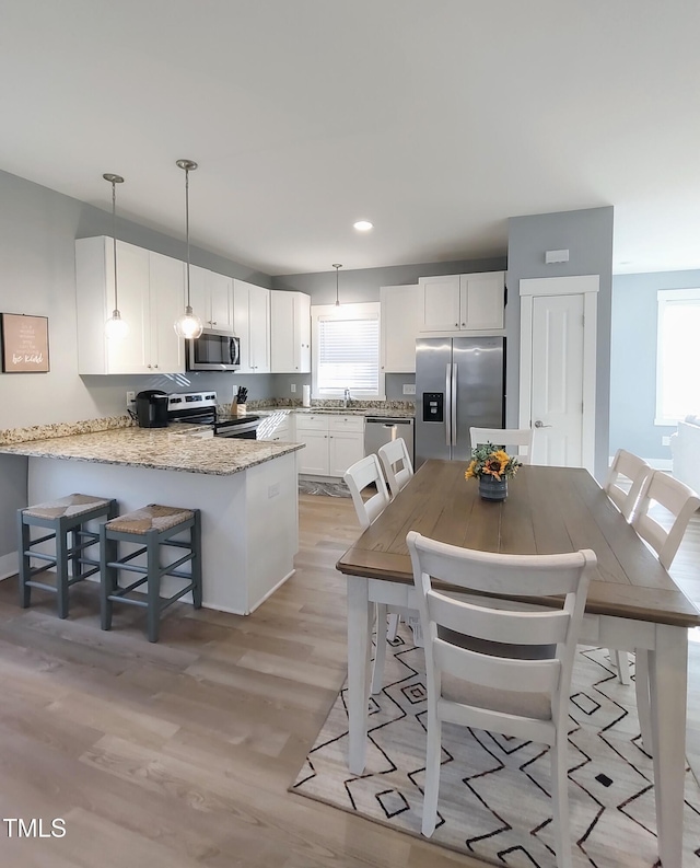 kitchen with stainless steel appliances, a peninsula, a sink, white cabinetry, and light wood-type flooring