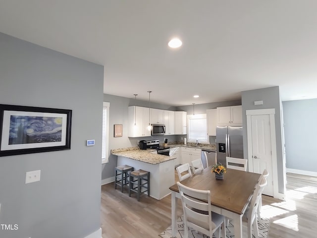 kitchen featuring light wood-style flooring, appliances with stainless steel finishes, white cabinetry, a sink, and a peninsula