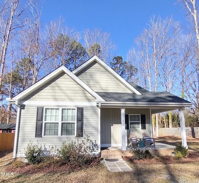 view of front of house featuring roof with shingles, a porch, board and batten siding, and fence