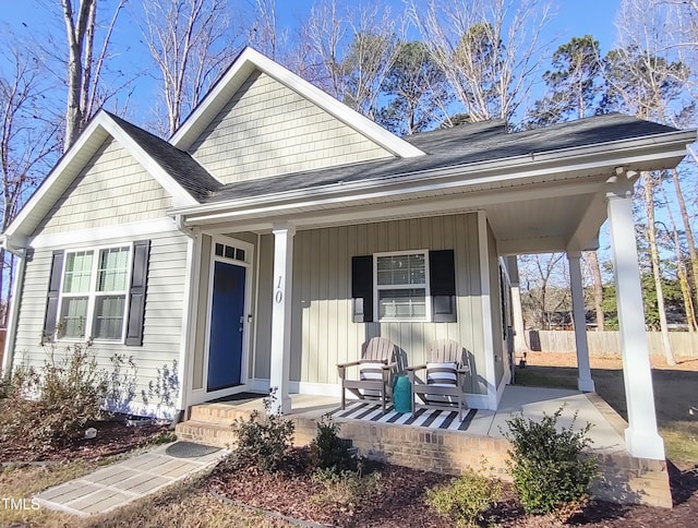 view of front of property with a porch, roof with shingles, fence, and board and batten siding